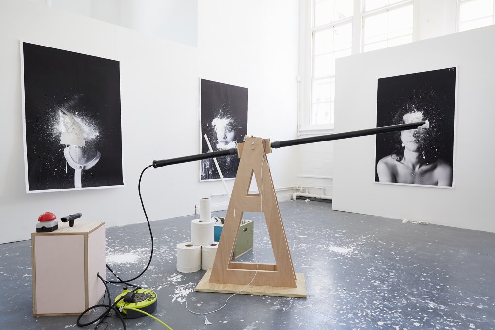 3 large scale black and white portraits surround an interactive air pump cannon which is used to fire paint at the portraits.     