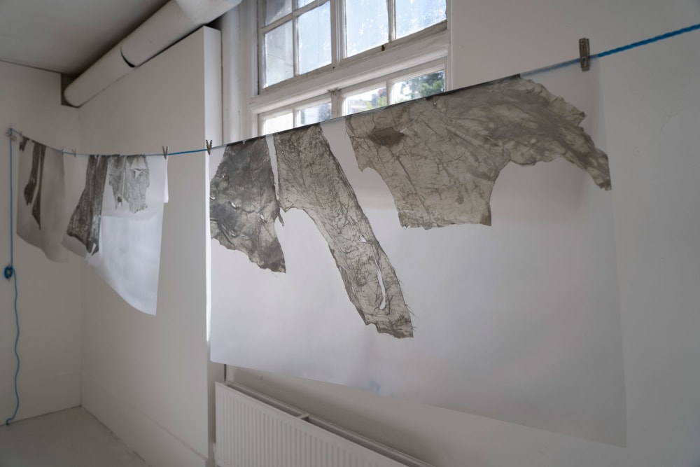 some paper prints hanging on a washing line inside a gallery space.