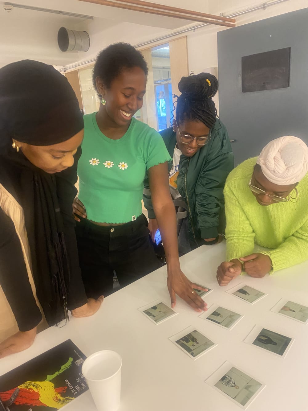 Photo of woman smiling wearing a green top, around a table with students. They are looking at photos on the table.