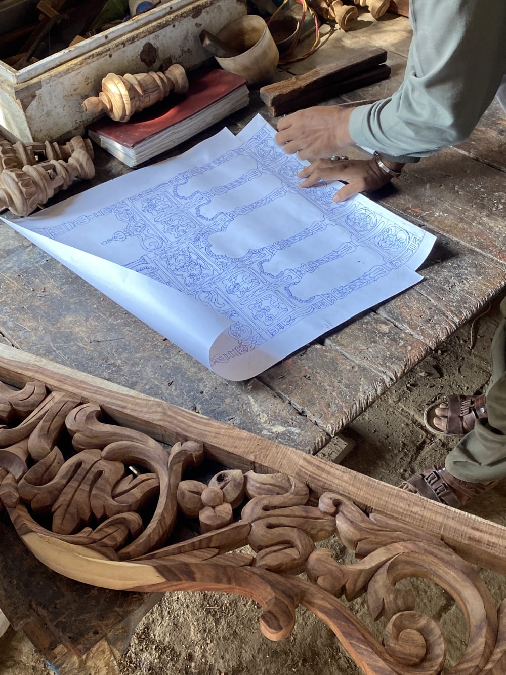 Detailed drawings on paper for a design of a shrine are laid on a table surrounded by sections of intricately crafted wood.