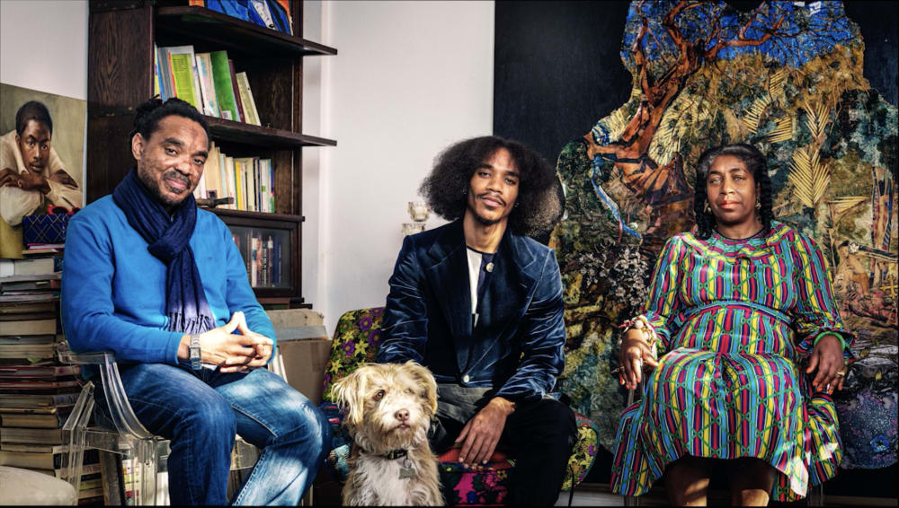 Student posing seat with his mum, dad and dog infrom of a bookshelf and artwork