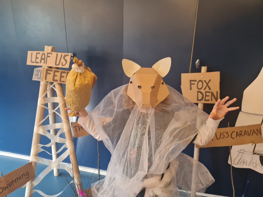 Child wearing mask shaped like a fox, making 'roar' expression with hands.