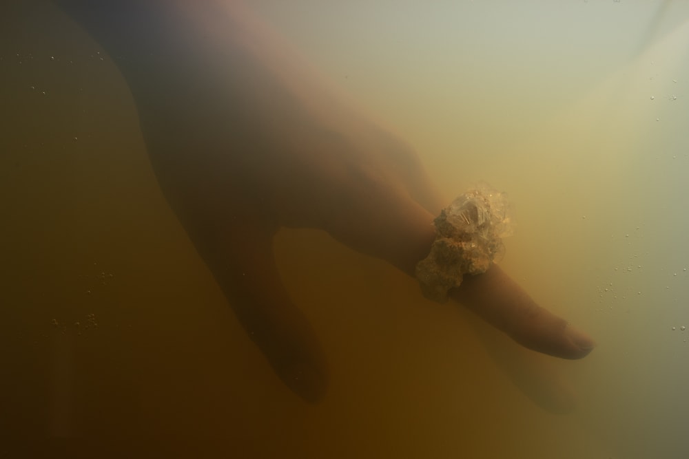 A blurry/ foggy image of a hand. Three fingers are visible and the index finger is adorned with a large crystal like ring. The image has moody green and amber tones