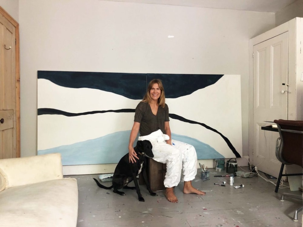 A woman and a dog sitting in front of a large, abstract painting.