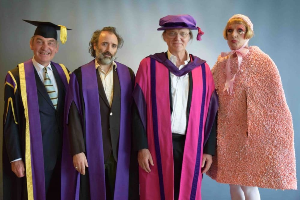 3 people in graduation gowns and Grayson Perry in a pink dress