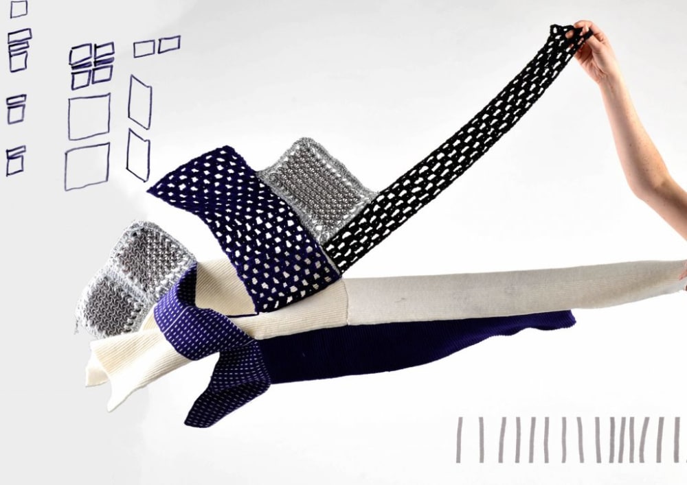 A blue, grey and white knitted garment being held up by a single hand.