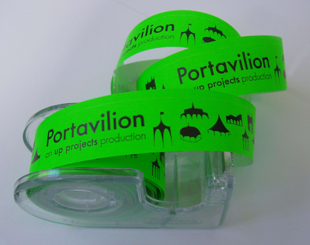 Photograph of a tape dispenser containing neon green tape printed in black with the words