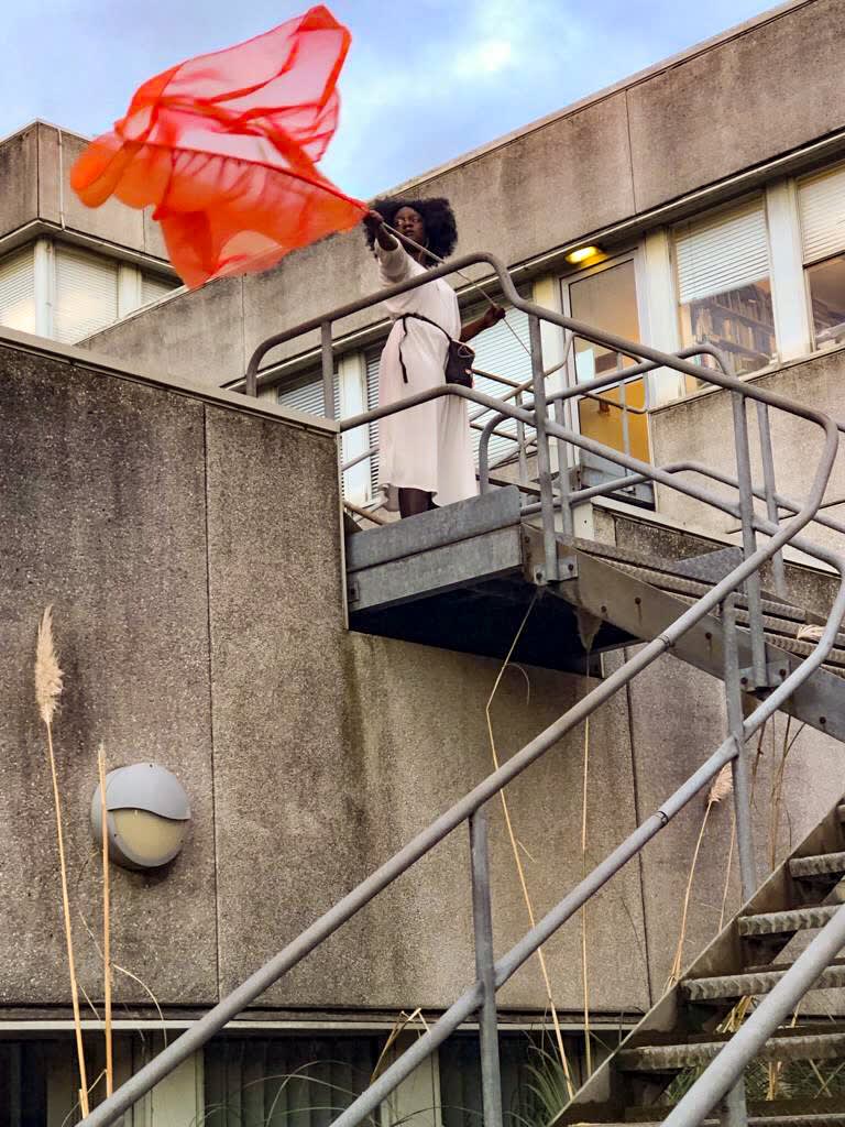Shot of performer standing at the top of an outside staircase waving a red flag