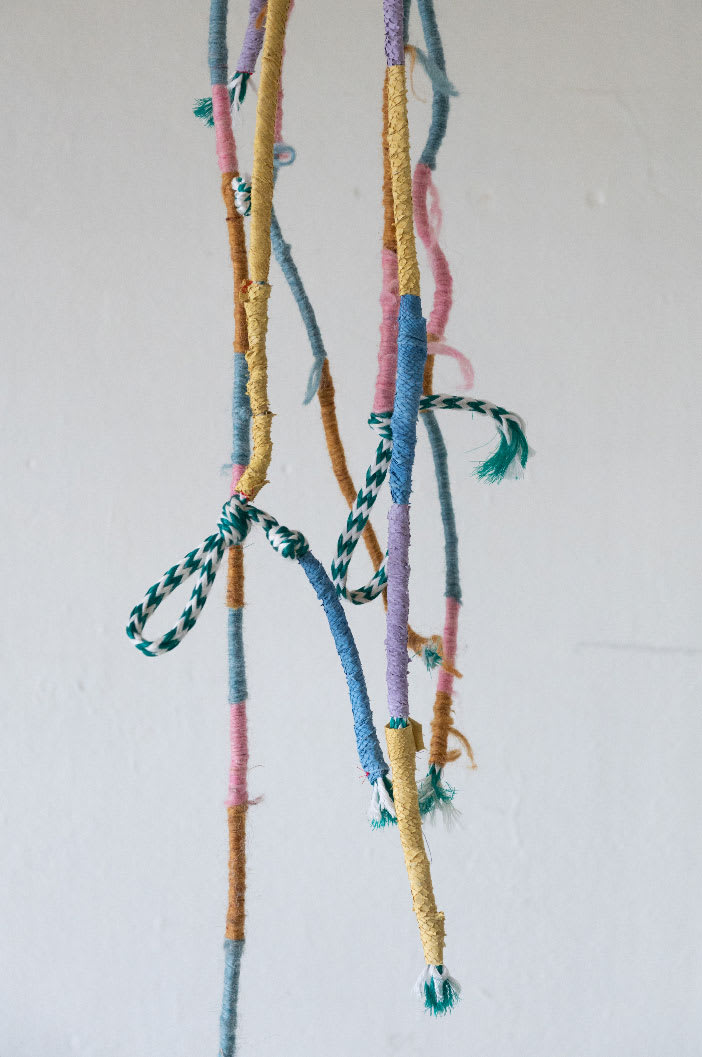 Multicoloured strands of ropes which have been woven and bound hanging against a white background.