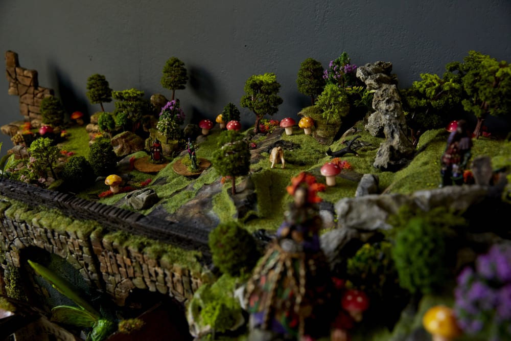 Image shows a miniature model of a forest with a train track going through the middle of the shot. There are spotted yellow and red mushrooms throughout