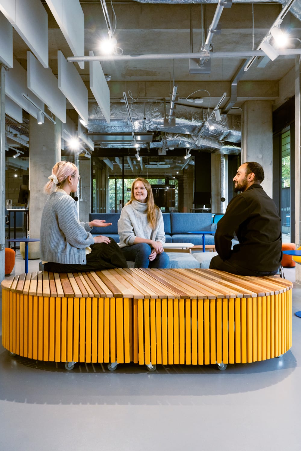 Three people are sat at The Hub talking, two of them are seated on the created bench
