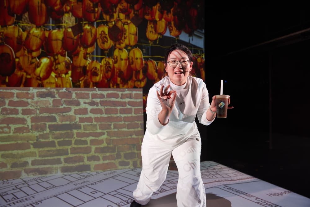 A woman is delivering a speech with bubble tea in her hand. Behind her is a screen filled with laterns
