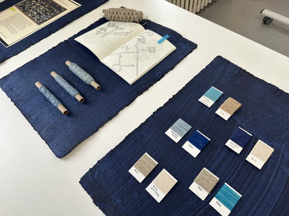 Samples of yarn are laid out, with a book of patterns placed on top of a dark blue cloth
