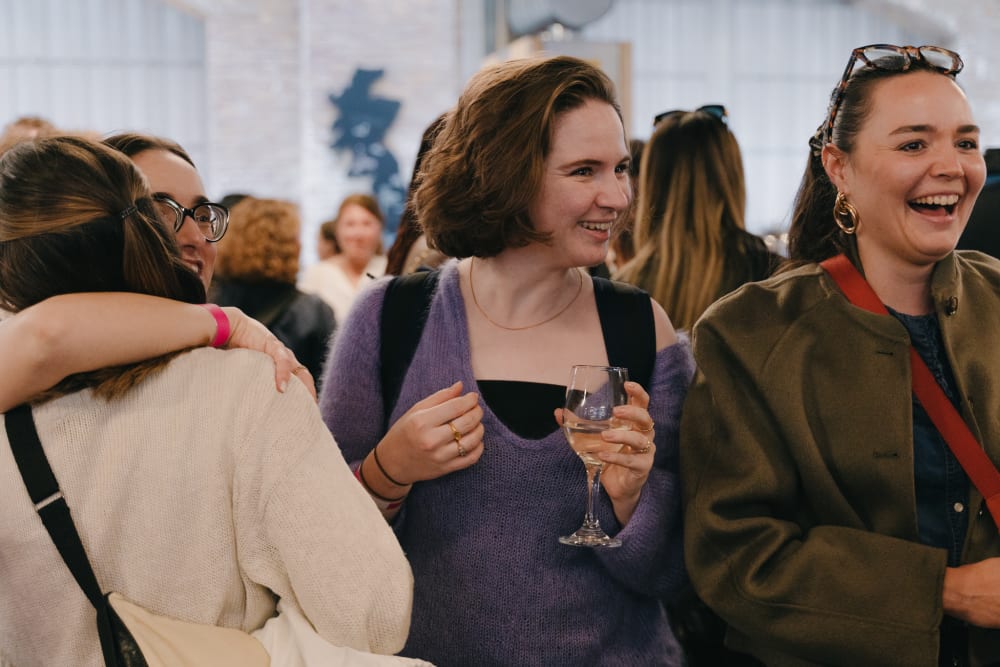 Guests stood smiling. 2 women are embracing to the left, and 2 are smiling next to them. 
