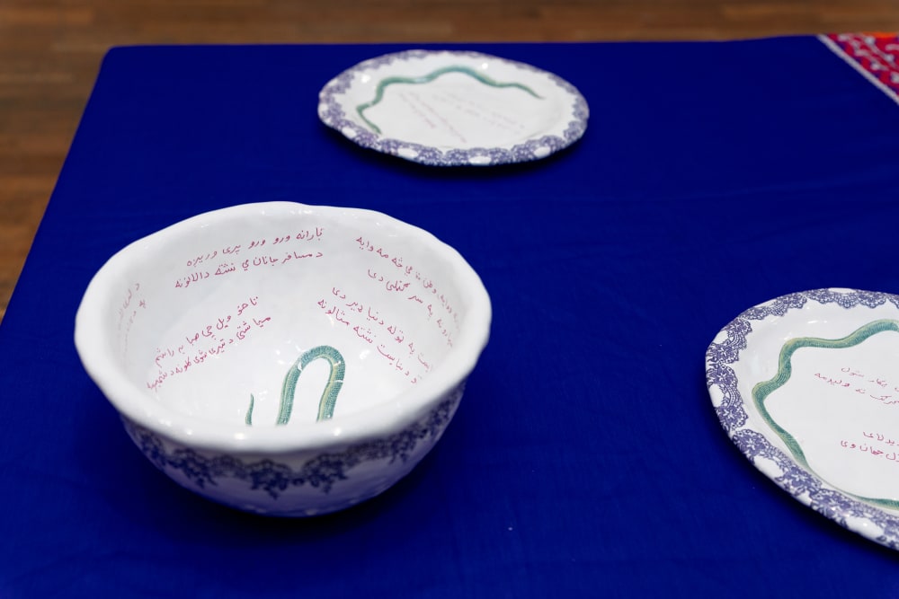 Close up of white, earthenware ceramic bowl and 2 plates with small green snakes painted in the centre and Arabic writing round the edges. 