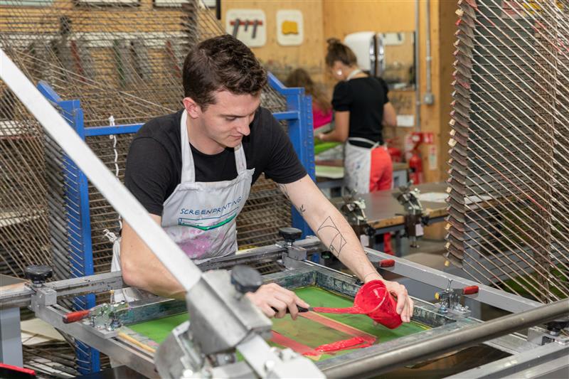 Student adding red paint onto print machine