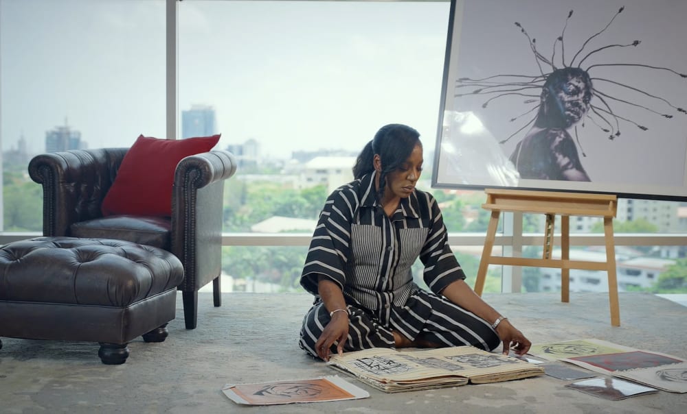 Itohan Barlow sitting in a room, looking at a big sketchbook