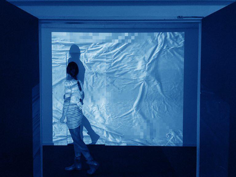 A woman walks in front of a projection of a sheet on a blank wall