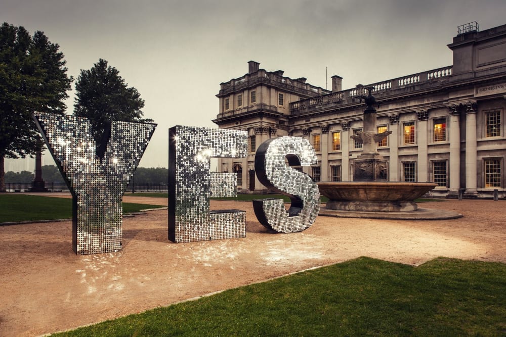 Sparkly, oversized sculpture of the word 'YES' in front of a stone building.