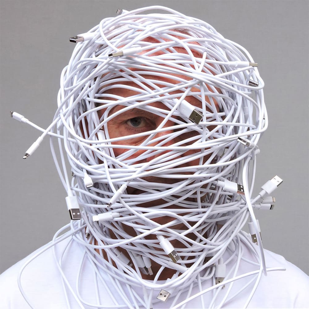 a man's head wrapping in iphone charger wires