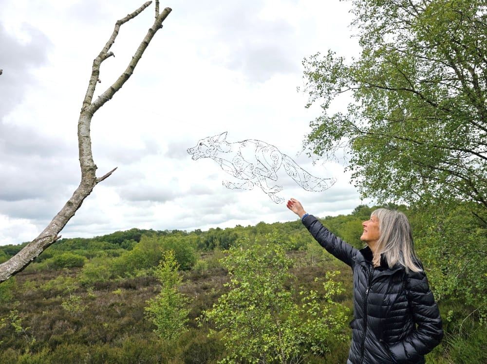linear wire sculpture of a fox floating in the air nex to a tree