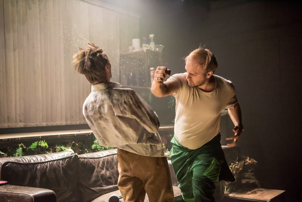 Two men standing face to face, one has just punched the other. The victim is moving backward from the force. The puncher has his fist clenched above his head and is leaning forward
