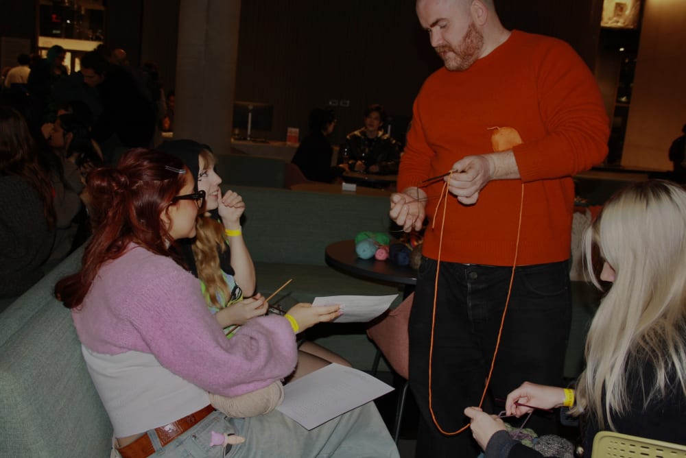 Person holding knitting speaking to two other people.