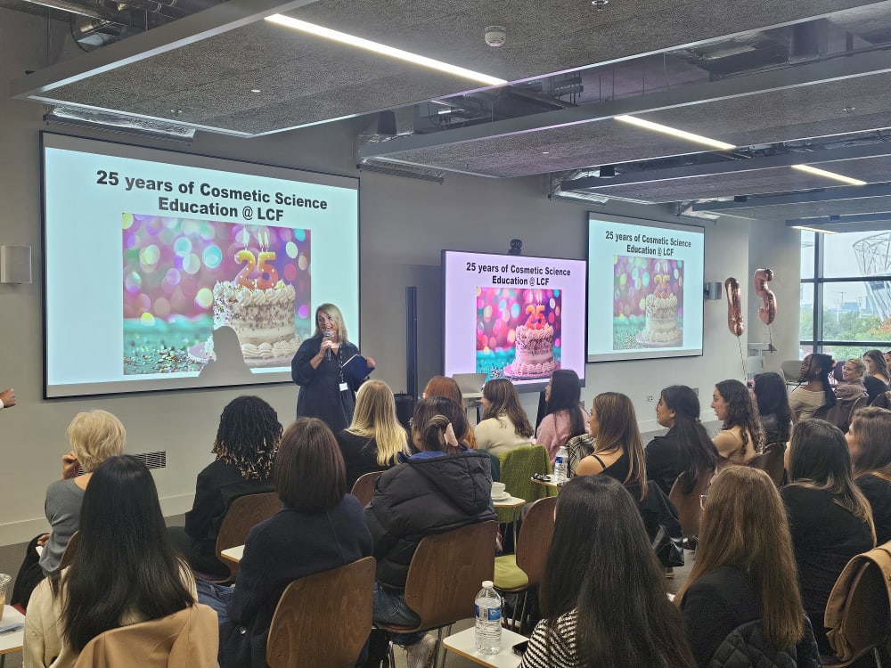 Dean of LCF Fashion Business School talking at the Cosmetic Science Industry Day, in front of 3 digital screens showing a birthday cake.