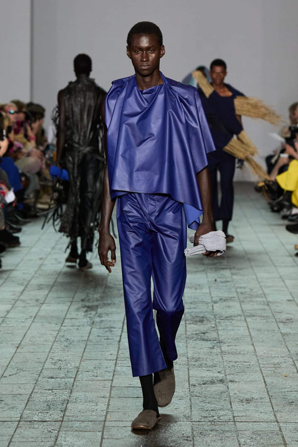 Image shows a black male model walking the catwalk dressed in silky blue material