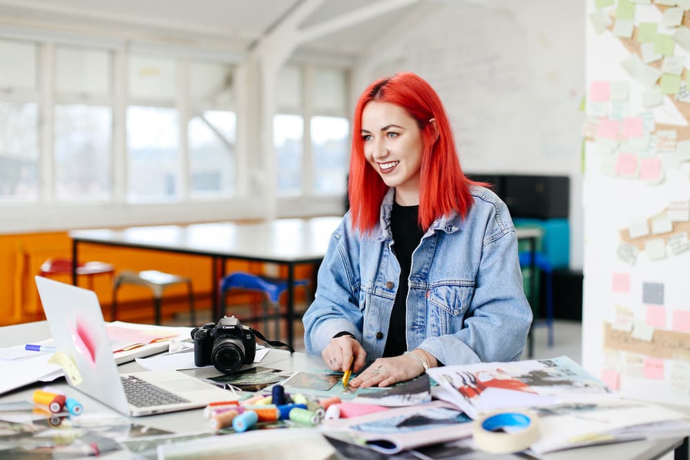 Female student with flame red hair sitting at table in studio