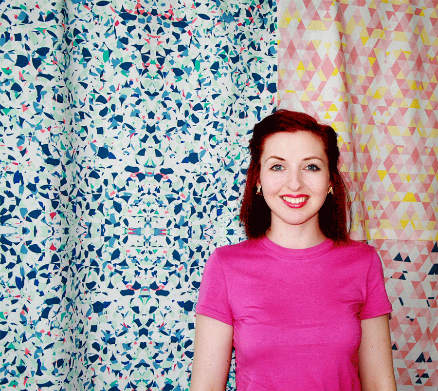 Woman wearing a pink t-shirt smiling to camera. Background is colourful material