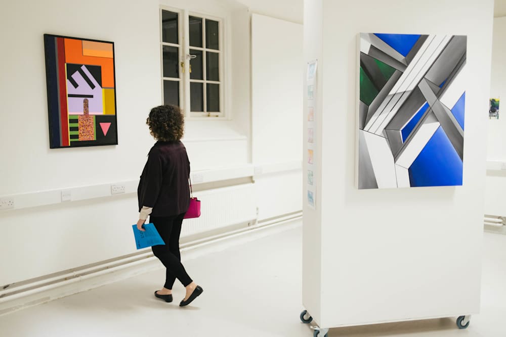 Photo of a woman at an art exhibit looking at the art. Her back is turned to the camera.