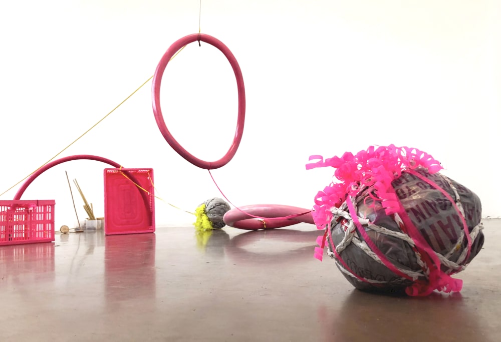 A room filled with large pink objects including a hoop, cube, crate and a ball made from rope and fabric.