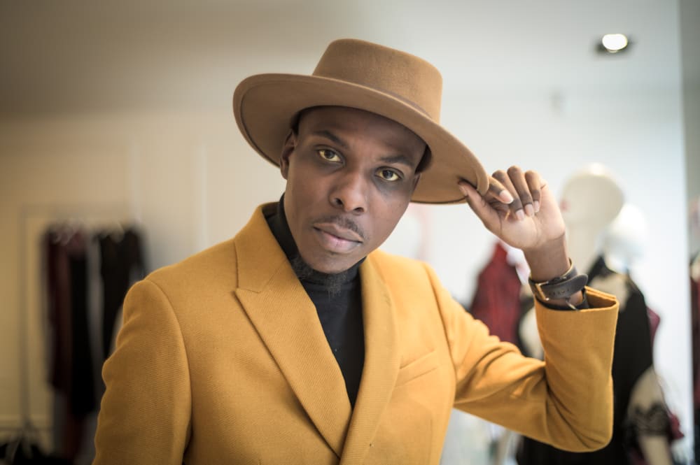 Man in yellow blazor, wearing a hat and looking into the camera