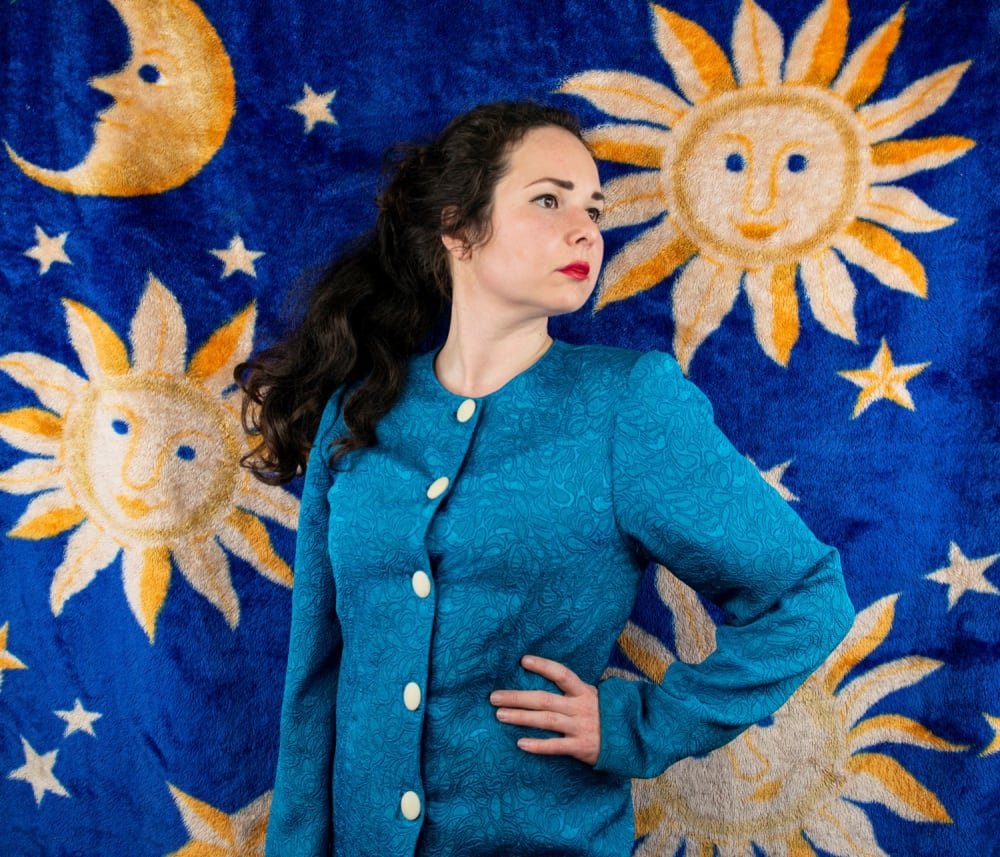 Woman standingin front of red velvet blanket holding a glass of wine