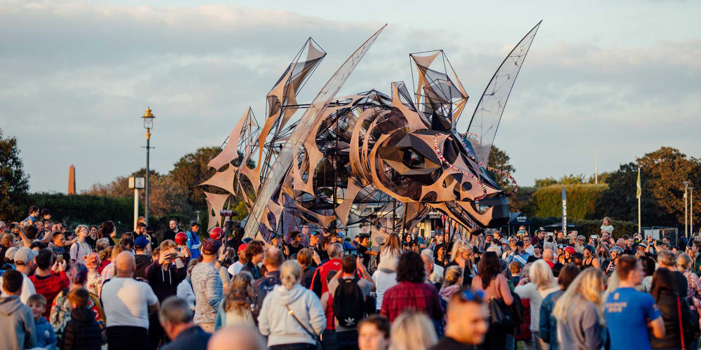 At dusk, a large puppet dragon dominates the scene in the middle and is surrounded by a crowd in the foreground and to the sides.  