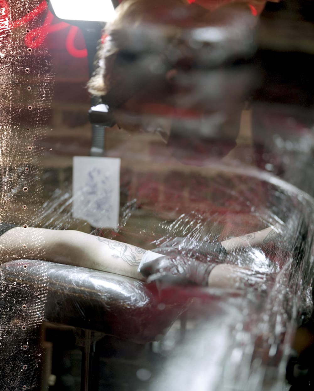 Hands wearing black surgical gloves wipe a freshly tattooed arm, they are cleaning it.