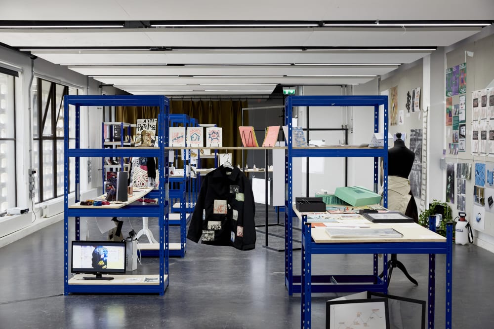 Image shows a large room with a blue metal bookcase in the middle. A black jacket can be seen hanging in the middle frame and there are books on top of the bookcase.