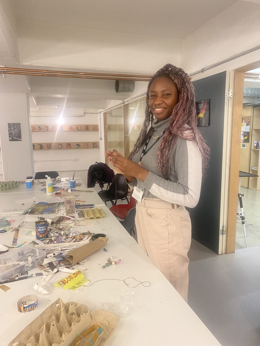 Woman smiling standing near a table with items to create beads from recycled goods.