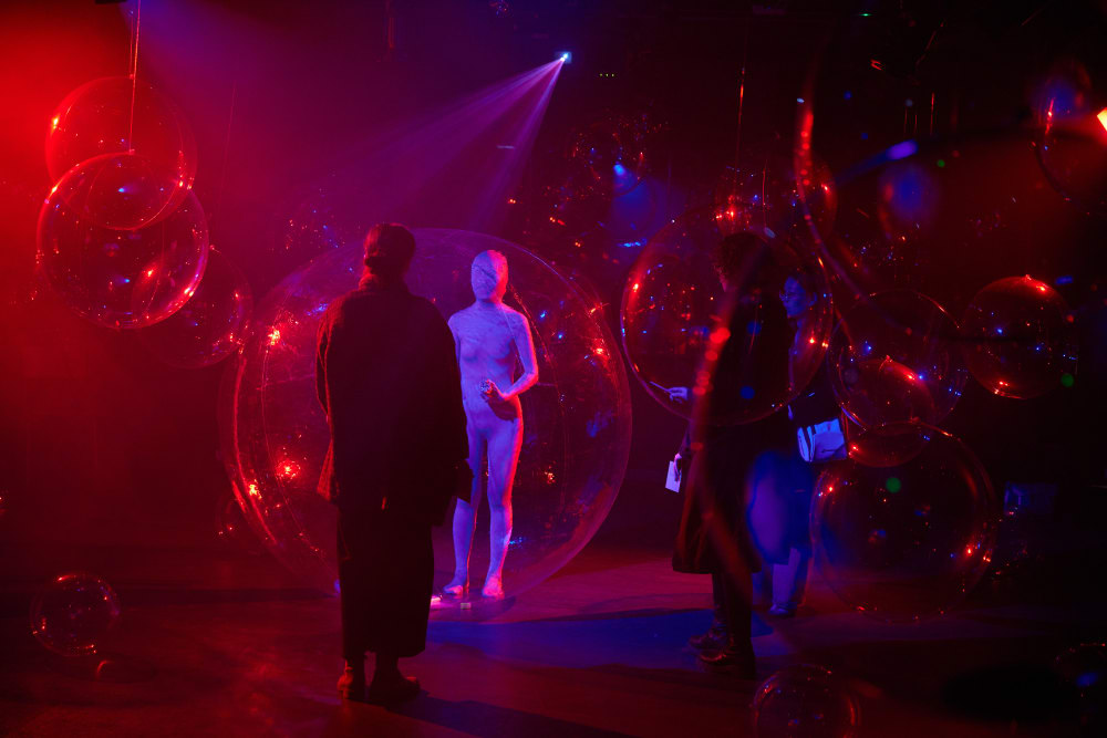 The room is full of red and purple lights and bubbles. There is a person in a white suit that covers their entire body and face