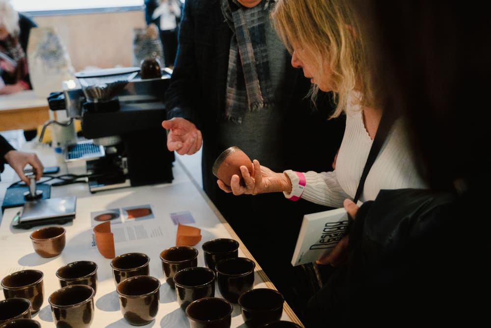 Guests looking at work on display. A woman is holding a small ceramic pot. 