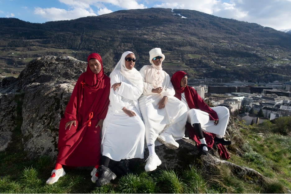 An outdoor shot of a group of friends in Muslim dress relaxed and perched on a rock against the Swiss landscape