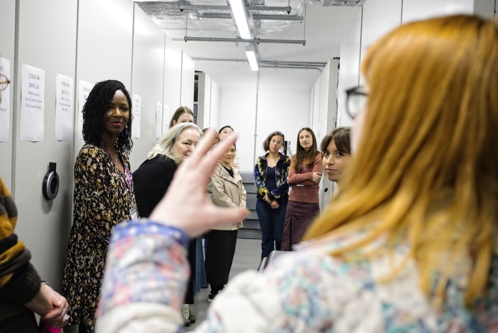Group of people standing in an archive listening to a person giving a speech.