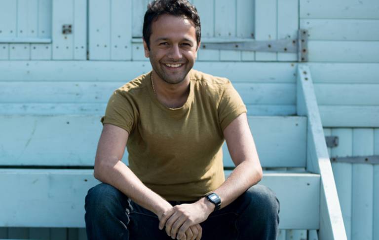 Man smiling and sitting on a wooden staircase outdoors.
