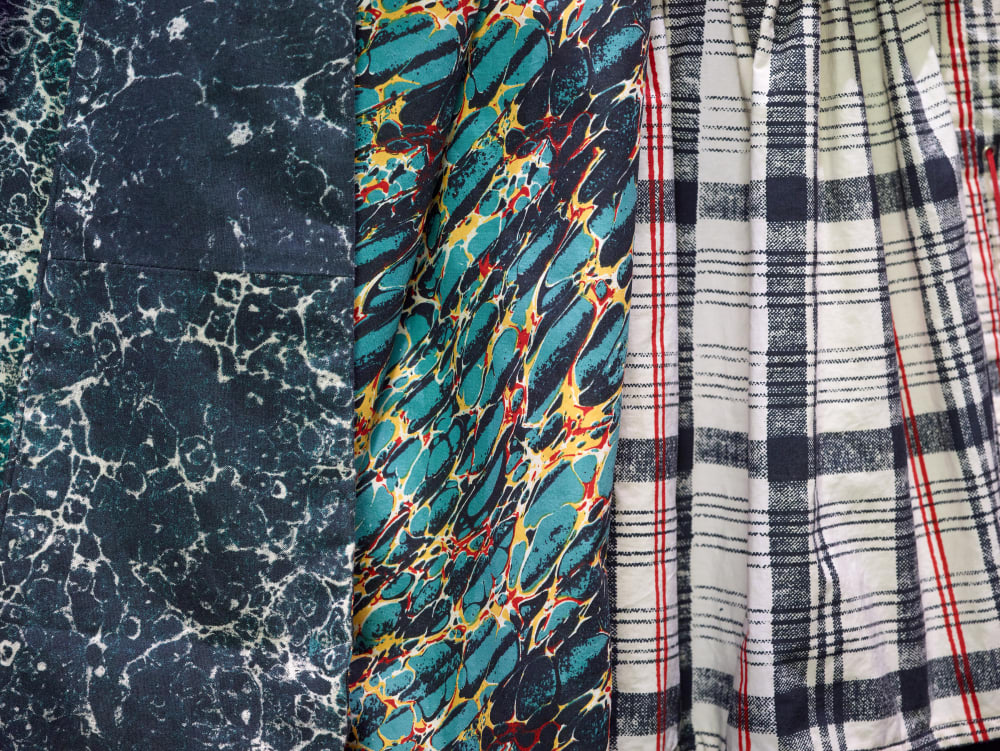 A close-up of three fabric patterns: dark blue with white marbling, vibrant green and red with yellow swirls, and black and red plaid on white.