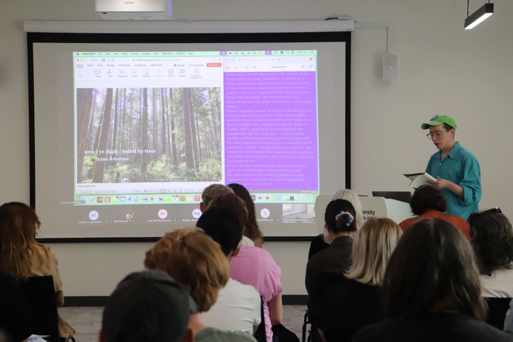Cannach MacBride reading a text to an audience. Backs of audience heads watching.
