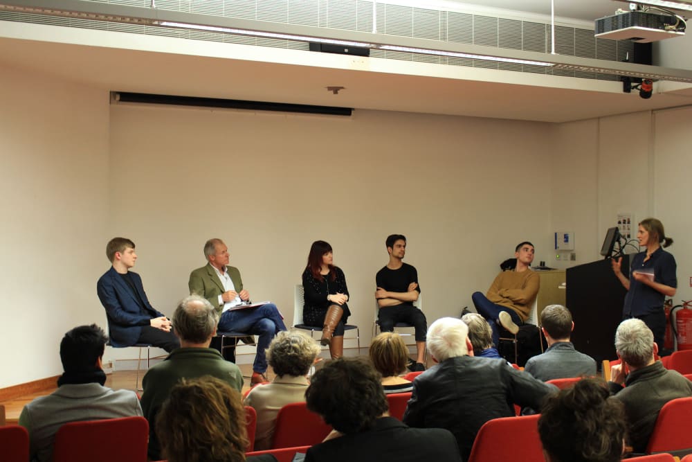six people sitting on a discussion panel on a stage