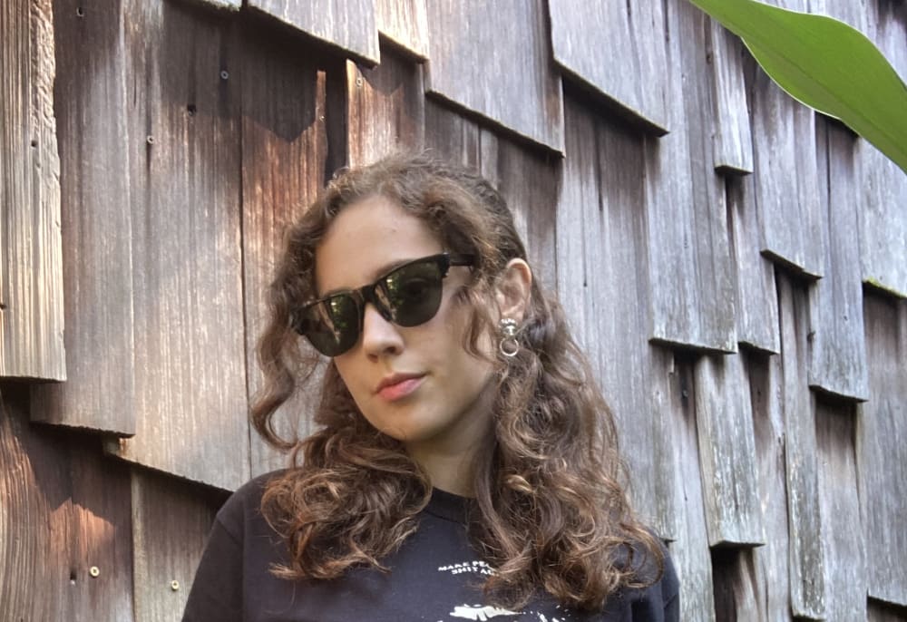 A photo of Ingrid Jensen wearing sunglasses, a black t shirt and a pair of denim jeans
