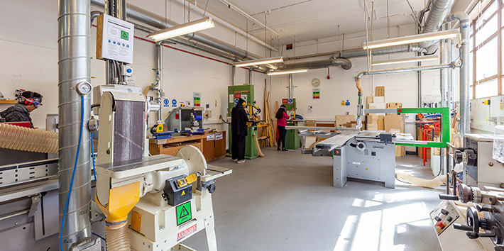Several students using pillar drills with the sanding machine and table saw also visible.