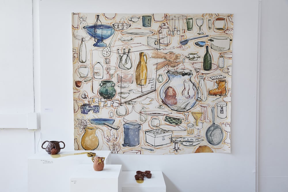 Three ceramic pieces are displayed on plinths. A watercolour, illustrative painting themed around ceramics is hanging on the wall behind the plinths.  